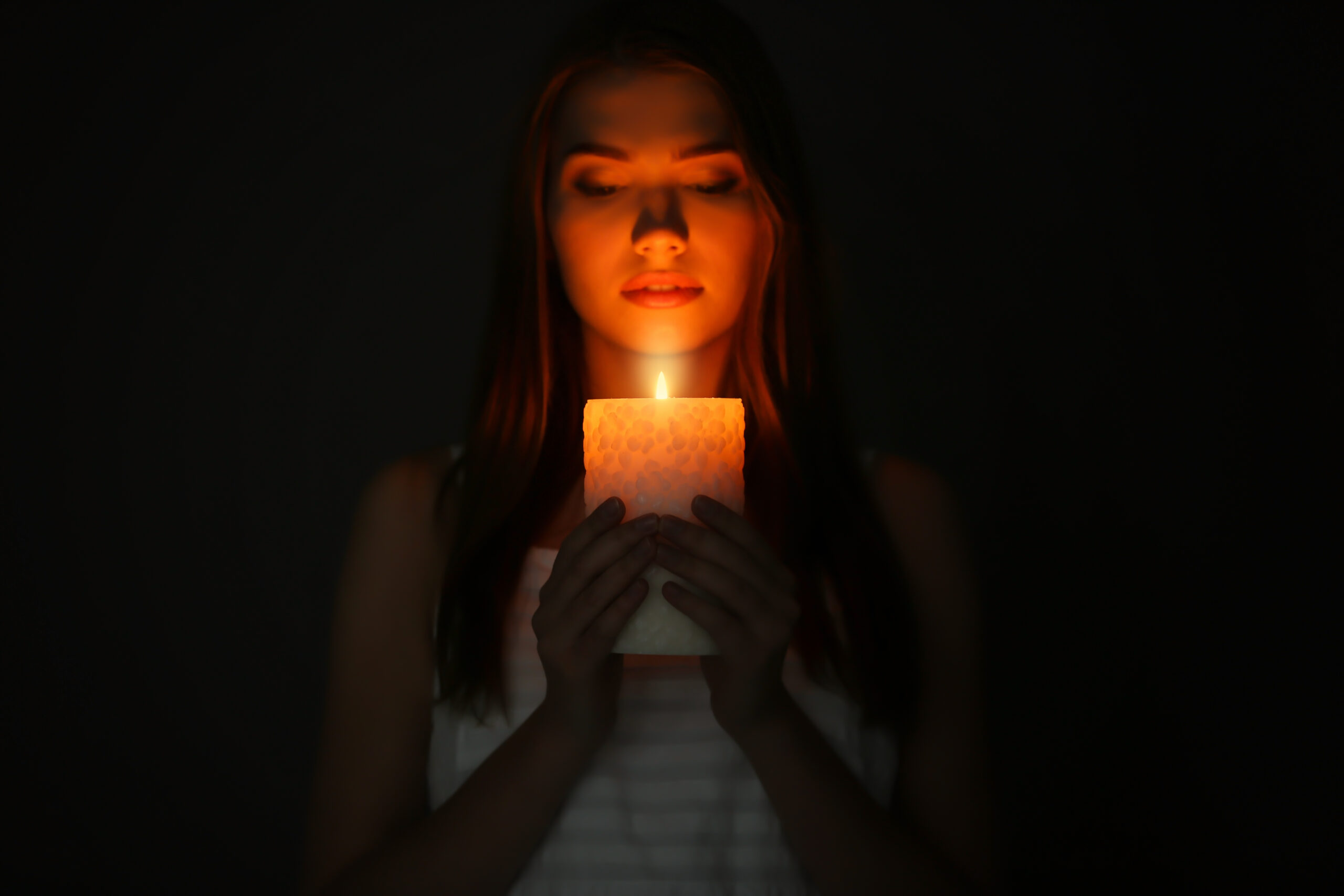 Beautiful young woman with burning candle in darkness